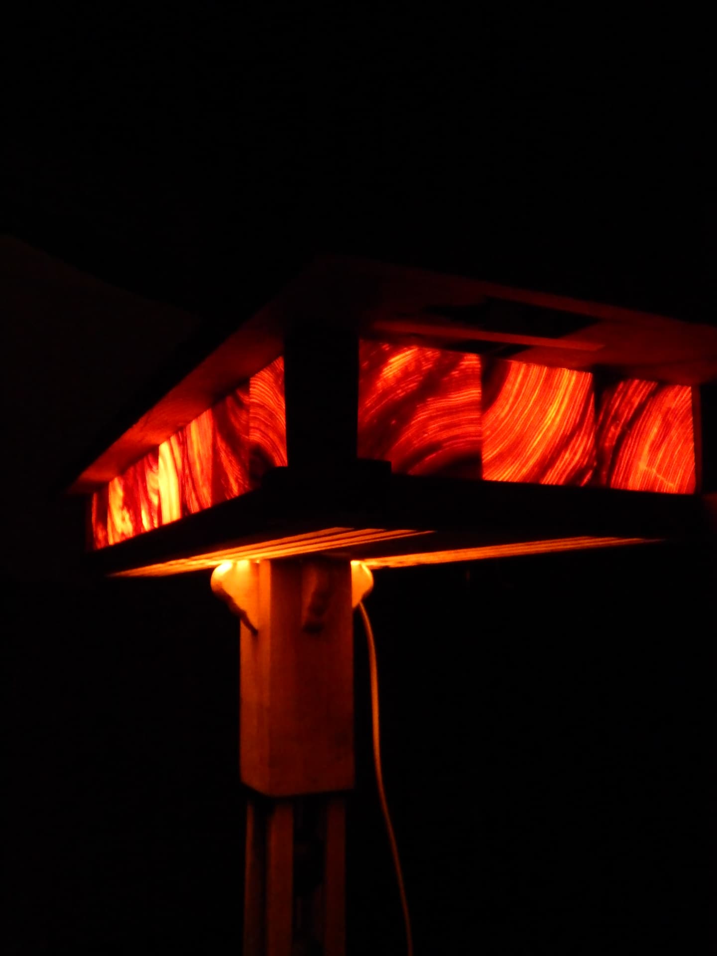 RIFT lamp glowing in darkness — resin panels radiating warm red light above a carved wooden column