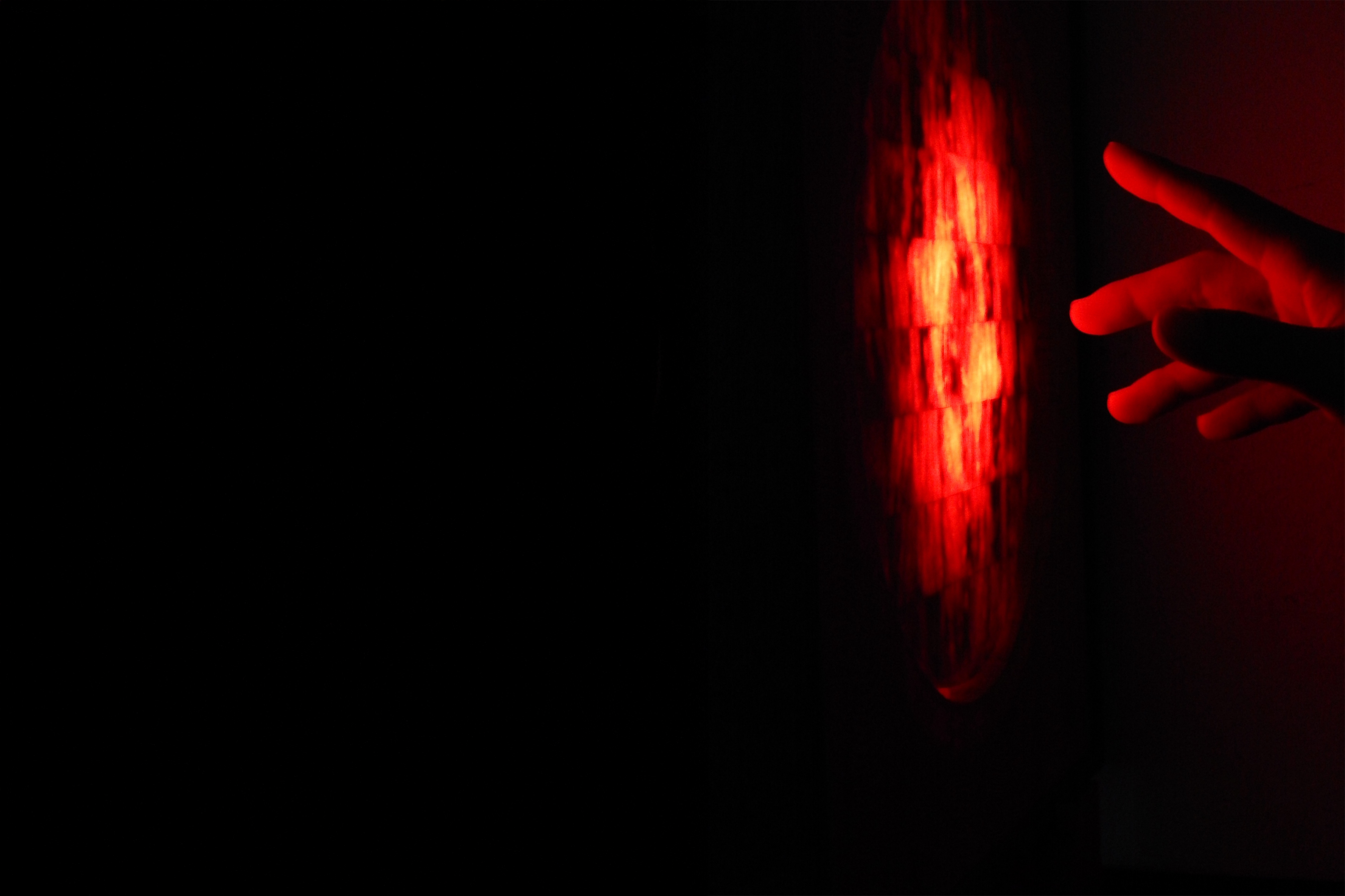 PULSE casting a warm red glow across a reaching hand in darkness
