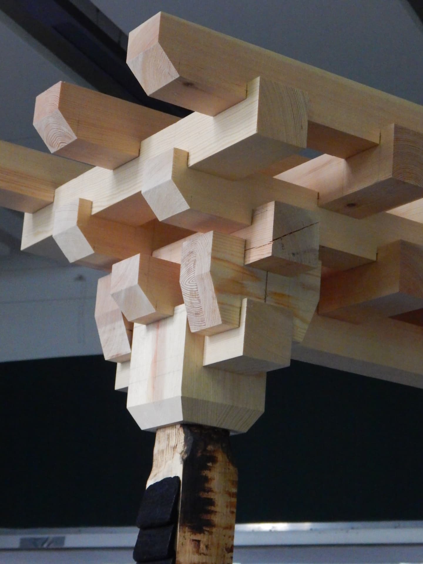 PASSAGE construction study — interlocking pale blocks gathered around charred timber